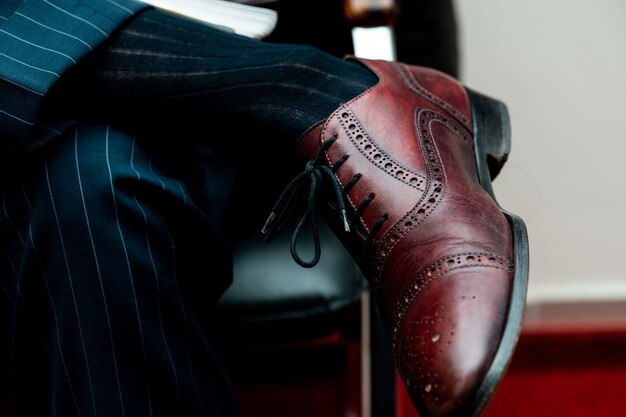 Closeup of a brogue shoe on a person sitting with crossed legs under the lights