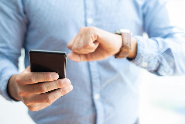 Closeup of business man holding smartphone and checking time