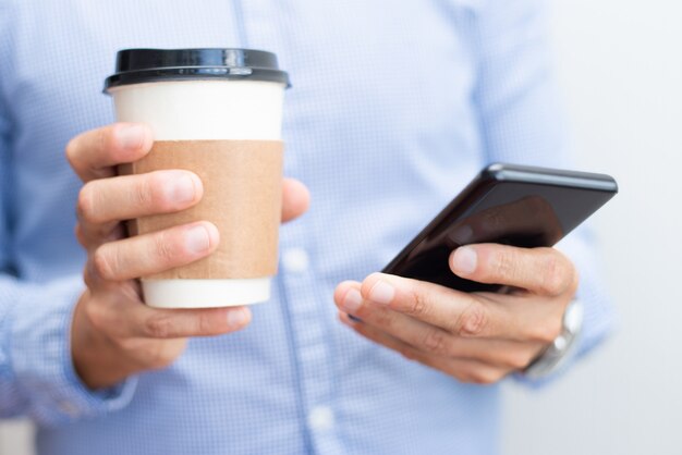 Closeup of business man holding smartphone and drink