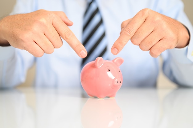 Closeup of a businessman pointing to a piggy bank