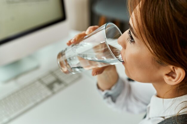 사무실에서 일하는 동안 물 한 잔을 마시는 사업가의 근접 촬영