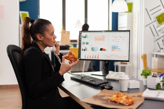 Closeup of businesswoman sitting at desk in front of computer eating pizza slice