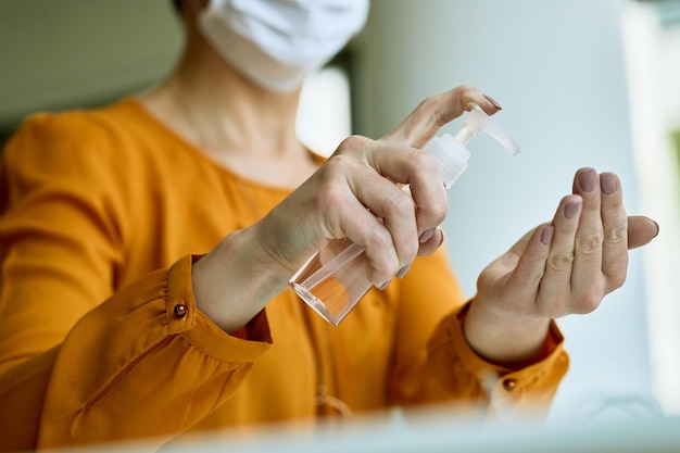 Closeup of businesswoman using using hands sanitizer while working in the office