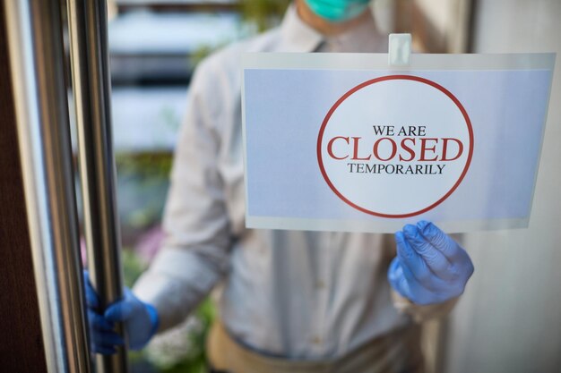 코로나바이러스 전염병으로 인해 문에 닫힌 표지판을 나눠주는 카페 주인의 클로즈업