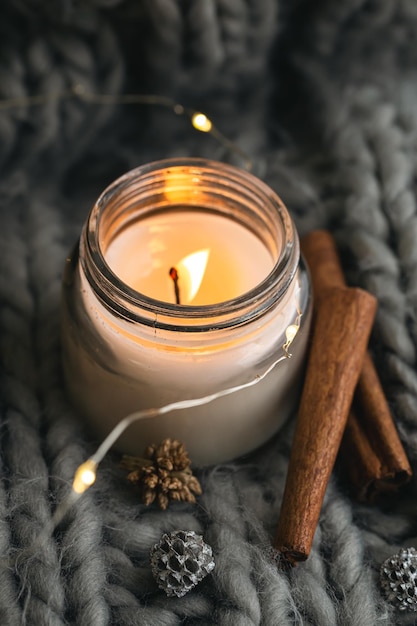 Closeup candle and cinnamon sticks on the background of a gray knitted element