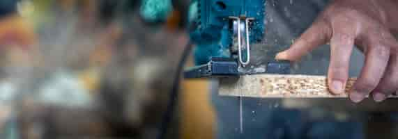 Free photo closeup of a carpenters hands in the process of cutting wood with a jigsaw