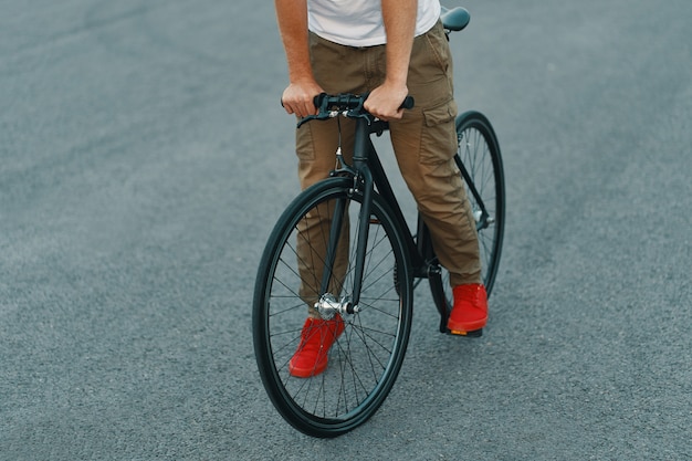 Primo piano delle gambe casuali dell'uomo che guidano bici classica sulla strada di città