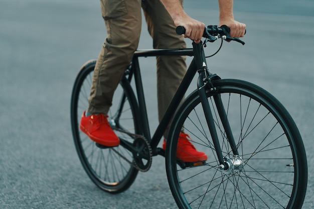 都市道路で古典的な自転車に乗ってカジュアルな男の足のクローズアップ