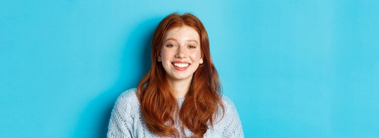 Бесплатный Фотография крупный план веселой девочки-подростка с рыжими кудрявыми волосами, счастливо улыбающейся в камеру, стоящую против синего б