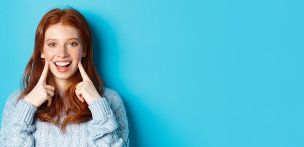 Closeup of cheerful teenage girl with red hair and freckles poking cheeks showing dimples and smilin