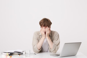 Closeup of cheerful young male student with braces wears beige shirt study using laptop computer and notebooks sitting at the table isolated over white wall