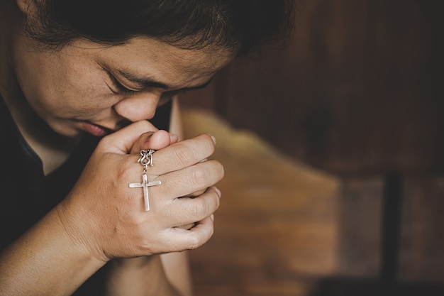 Closeup of christian senior woman hands holding crucified cross while praying God.