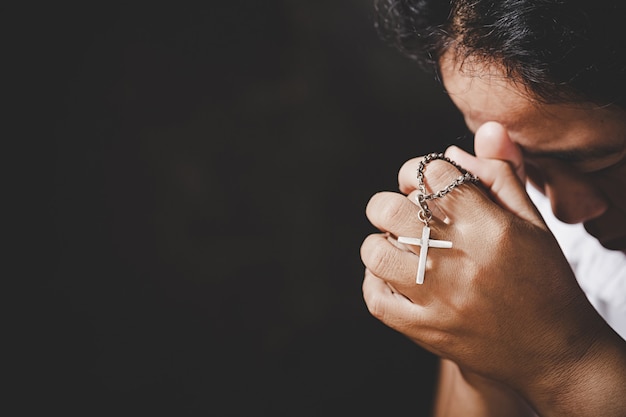 Closeup of christian senior woman hands holding crucified cross while praying God. 