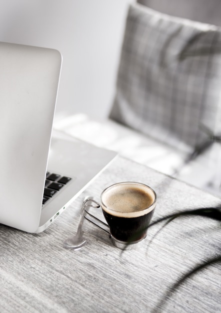 Closeup of a coffee on a table with a spoon and a laptop on the side