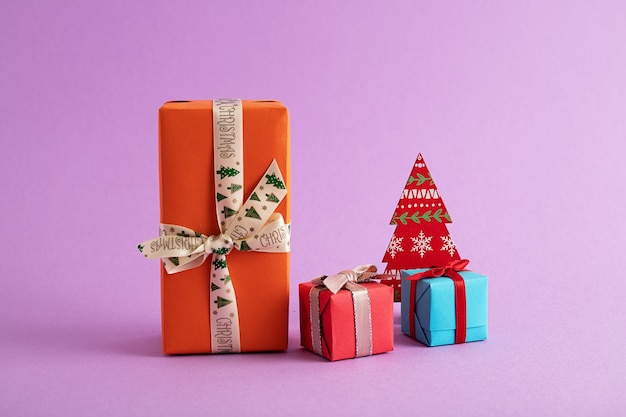 Closeup of colorful gift boxes and a paper Christmas tree in the purple background