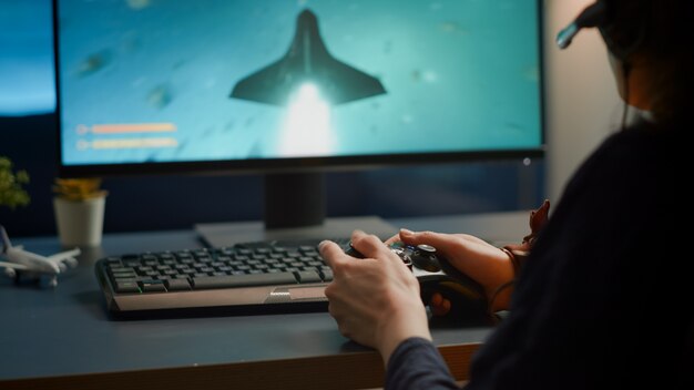 Closeup of competitive woman player holding joystick playing space shooter video games at powerful computer late night. Professional gamer using wireless controller for online gaming championship