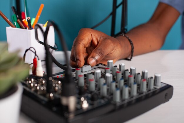 Closeup of content creator hand adjusting master volume fader on mixer console on desk during live podcast. Vlogger working on sound settings of equilizer used to broadcast live stream.