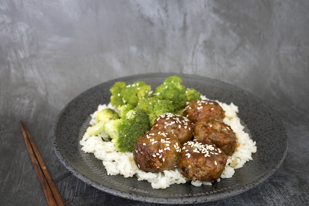 Closeup of cooked rice with meatballs and broccoli in a plate on the table