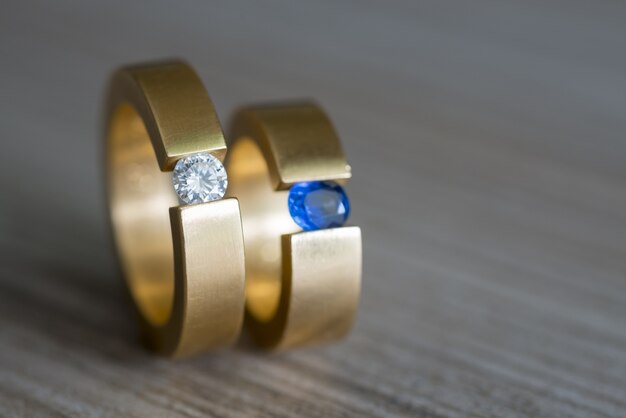 木製のテーブルにダイヤモンドとサファイアのカップルの黄金の結婚指輪のクローズアップ