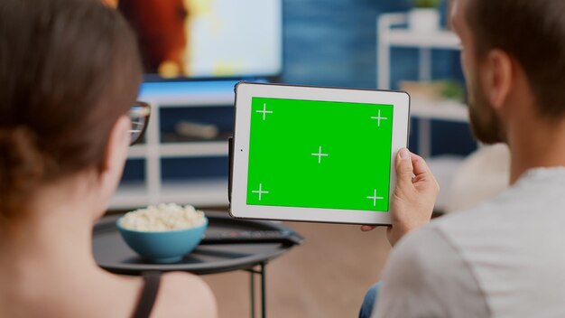 Closeup of couple holding digital tablet with green screen watching webinar and talking
