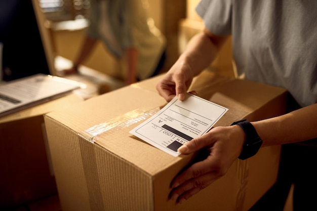 Closeup of courier attaching address label on a package while working in the office