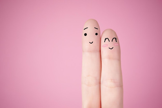 Closeup of cute faces doodled on fingers against a light pink background