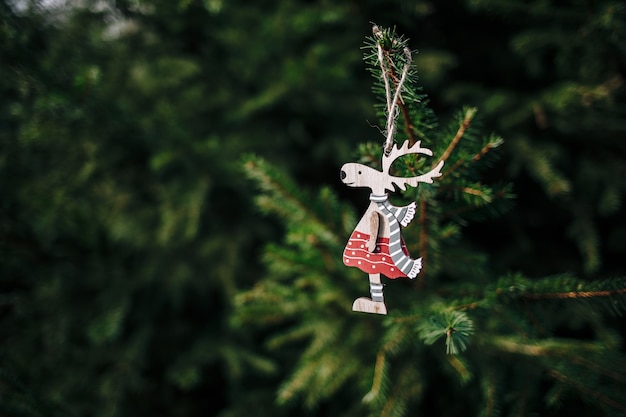 Closeup of a cute wooden deer-shaped Christmas ornament hanging from a pine tree