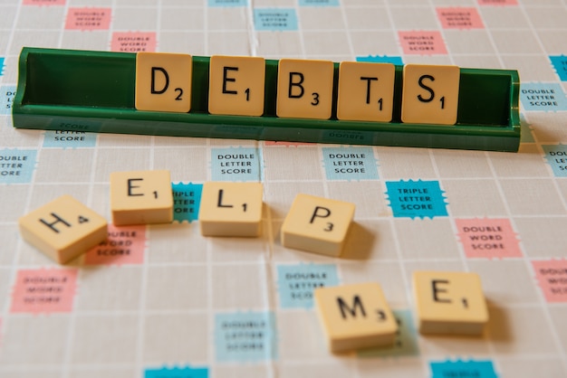 Free photo closeup of debts and help me written on a scramble board under the lights