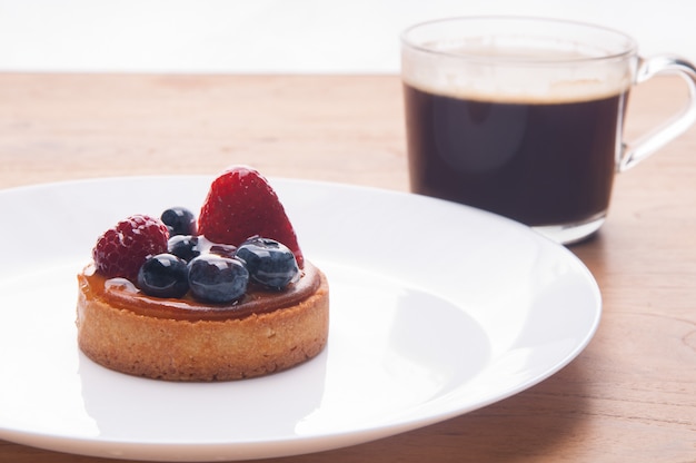Closeup of delicious mini tart with berries and cup of coffee