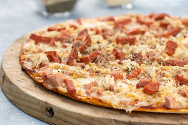 Closeup of a delicious pizza with sliced sausages and melted cheese on a board under the lights