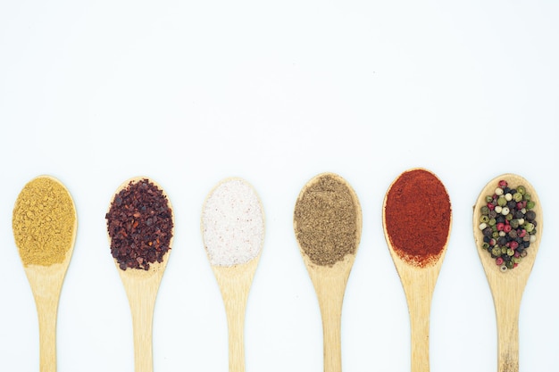 Closeup of the different types of spices with wooden spoons isolated on white background