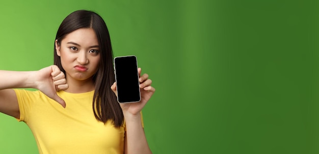 Free photo closeup disappointed upset asian girl judging bad awful app show smartphone screen thumbdown grimaci