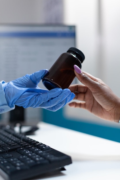 Closeup of doctor hand giving pills bottle to african american sick patient discussing medication treatment against sickness during clinical appointment. Physician woman working in hospital office