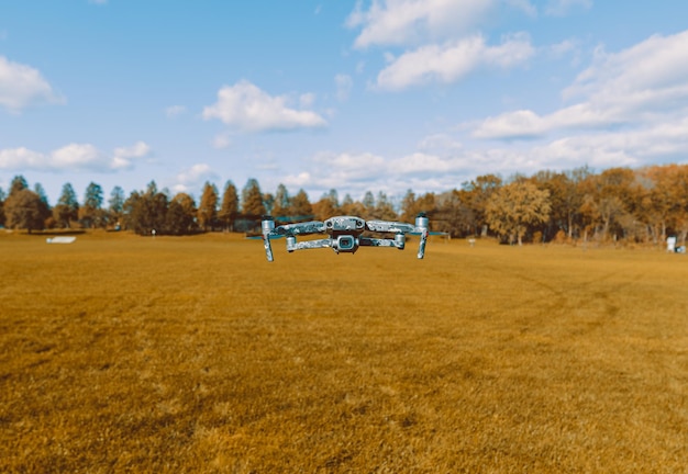 Closeup of a drone flying over a green field next to a forest