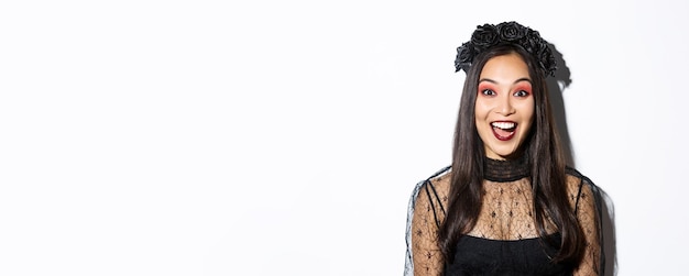 Free photo closeup of enthusiastic asian woman looking amused wearing witch costume on halloween standing over