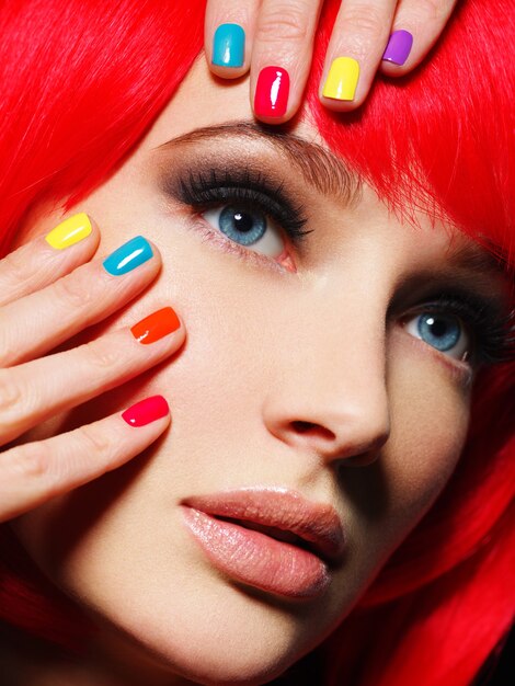Крупным планом лицо красивой девушки с яркими разноцветными ногтями.