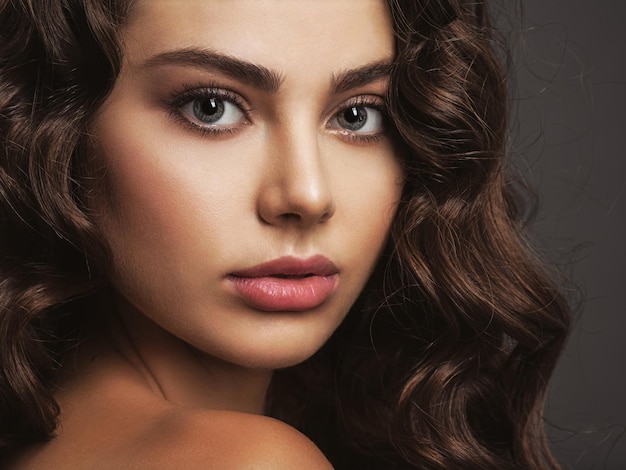 Closeup face of a beautiful woman with a smoky eye makeup. Sexy and gorgeous brown-haired woman with long curly hair. Portrait of an attractive female posing .
