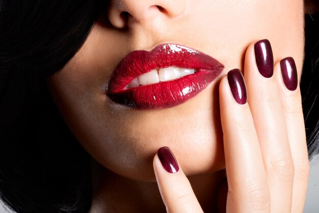 Closeup face of a woman with beautiful sexy red lips and dark nails