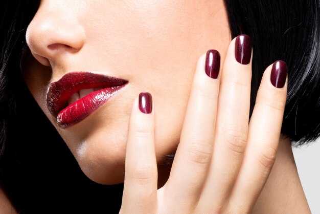 Closeup face of a woman with beautiful sexy red lips and dark nails 