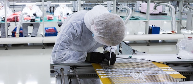 Free photo closeup of a factory worker in a white lab suit and black latex glove working with a soldering iron and some modern equipment other workers are on the background