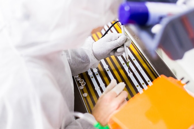 Foto gratuita primo piano di un operaio in una tuta da laboratorio bianca e guanti in lattice seduto sulla sedia e che installa i led in un televisore con un saldatore