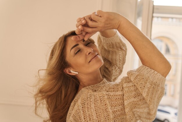 Closeup of fairskinned adult lady in warm sweater posing with her eyes closed in bright room near window Rest time concept