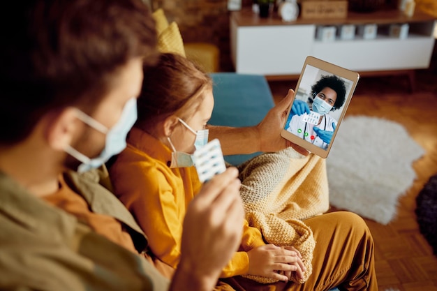 Closeup of father with ill daughter consulting a doctor via video call about prescription medicines during coronavirus pandemic
