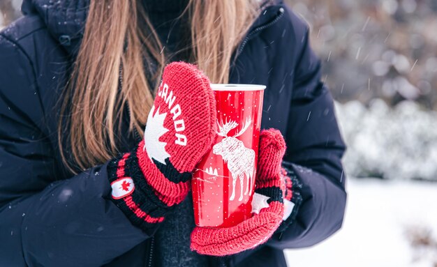 Closeup of female hands in canada mittens hold a red thermal cup