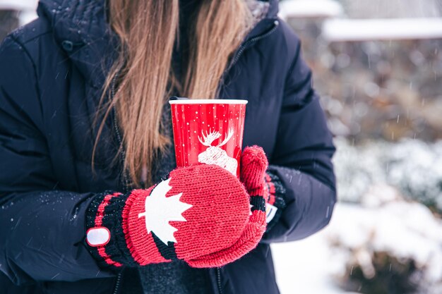 カナダのミトンの女性の手のクローズアップは赤いサーマルカップを保持します