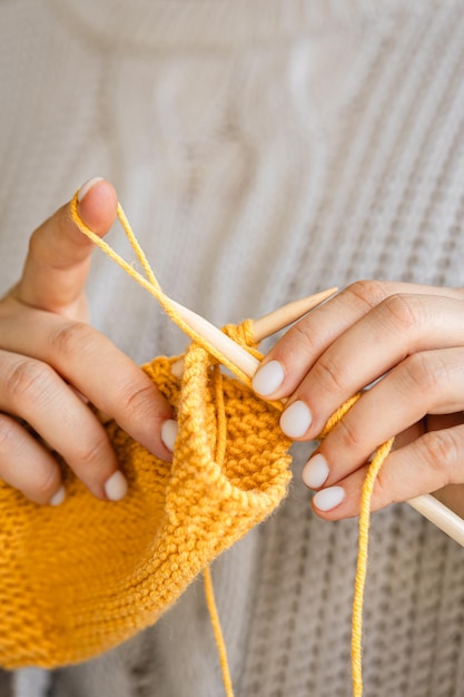 Free photo closeup of female hands knitting yellow wool sweater