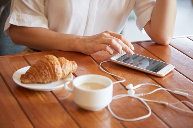 朝のコーヒーを飲みながらスマートフォンでメッセージをテキストメッセージの女性の手のクローズアップ