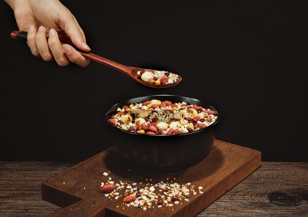 Closeup of the female's hand holding a wooden spoon of grain soup ingredients on a black bowl