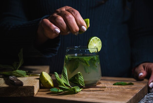 Closeup of a female squeezing a lemon into a glass of lemonade with mint drinks