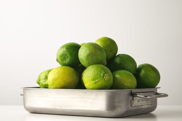 Closeup of fresh limes in a steel saucepan isolated on the white table.